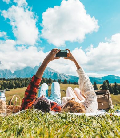 Couple of tourists lying on the grass visiting tirol alps. Boyfriend and girlfriend in love taking a photo of the mountains landscape with vintage camera - Vintage filter - Wanderlust concept